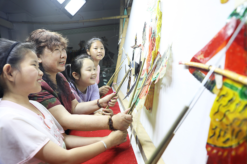 皮影藝人指導(dǎo)小朋友表演皮影戲。